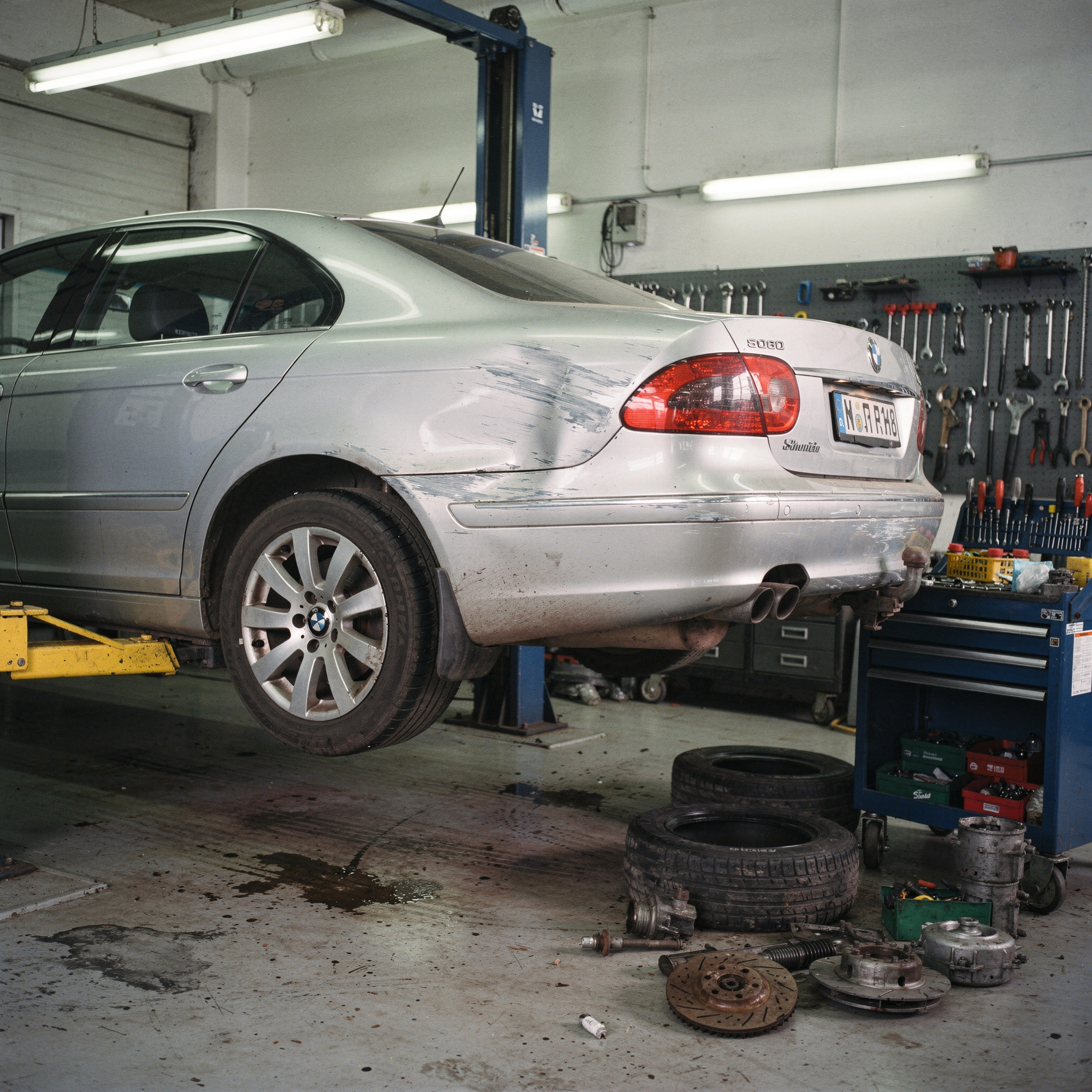 Deformierter Kotflügel eines silbernen Autos auf einer Hebebühne in einer Kfz-Werkstatt.